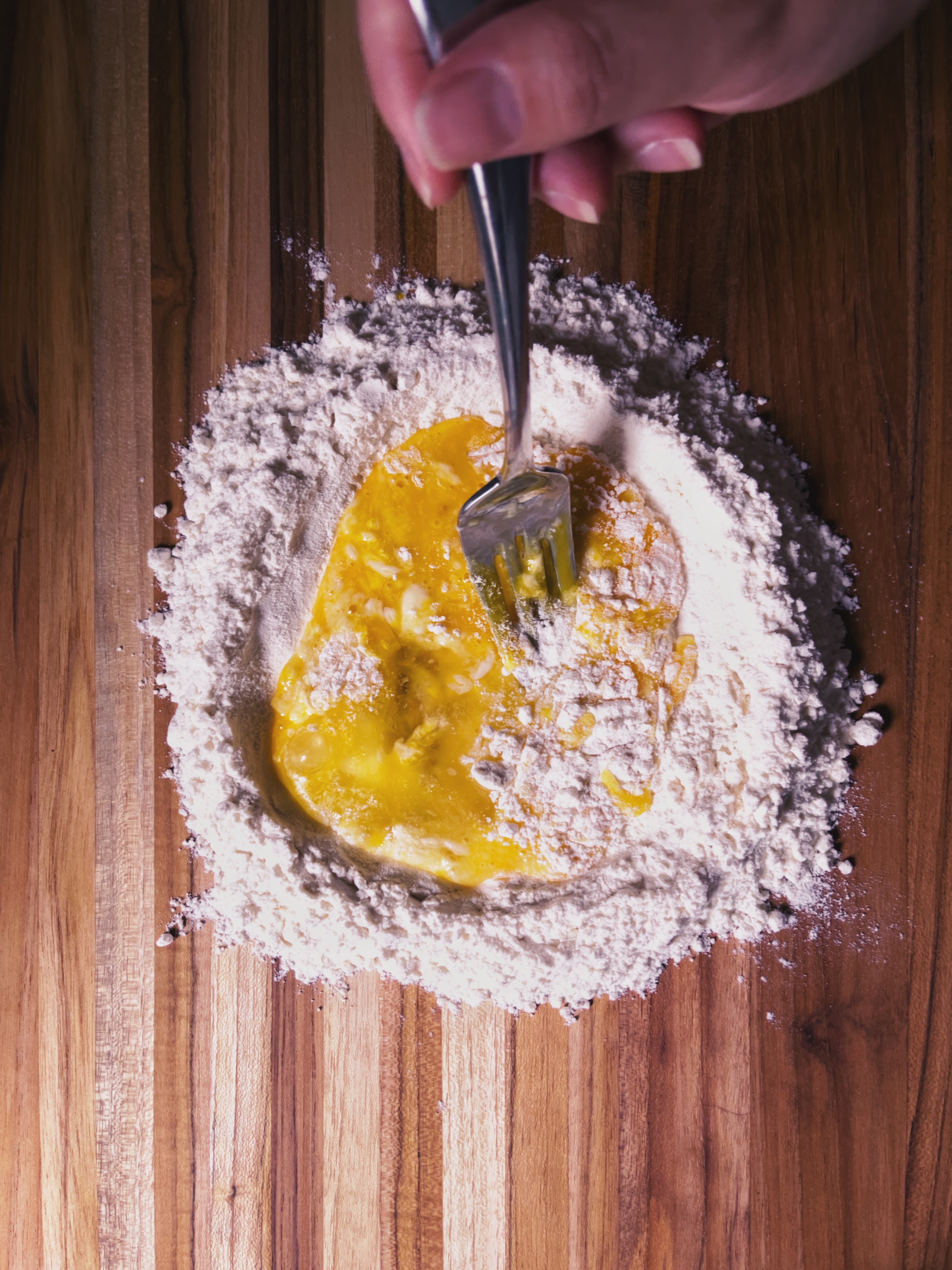 making pasta: mixing flour and eggs on wooden board